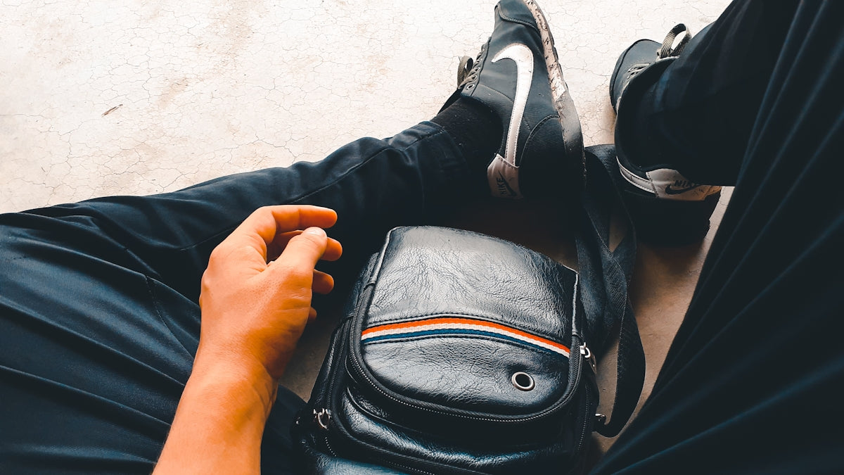 man in blue pants and pair of black and white Nike sneakers with black leather crossbody bag