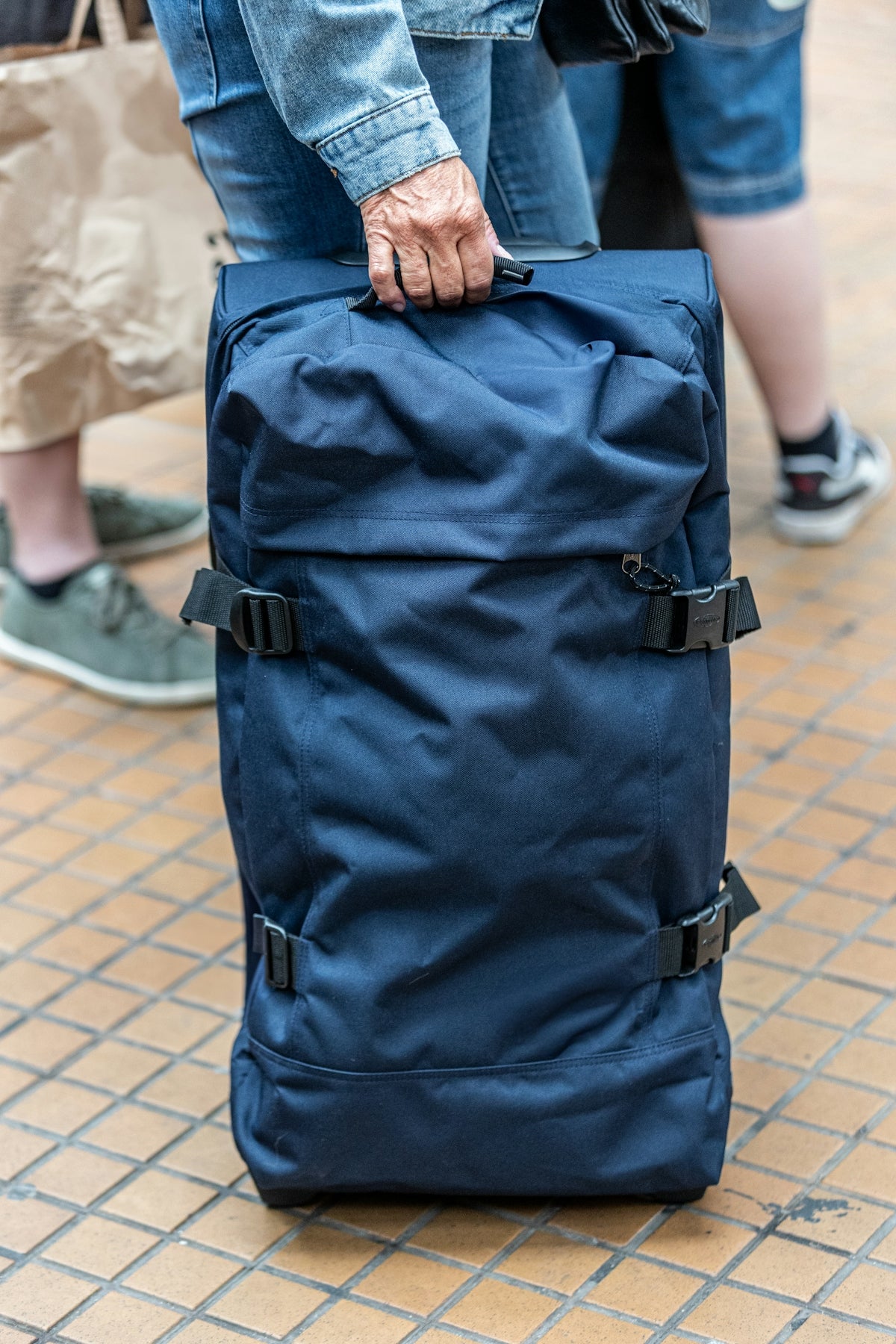Person holding a large navy blue duffel bag with wheels.