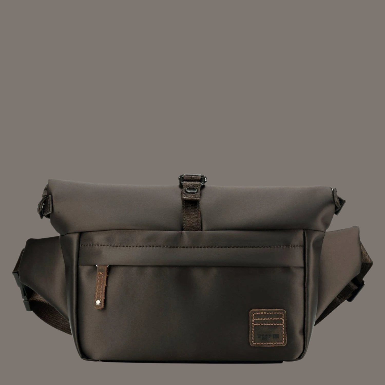 dark brown waist bag or sling bag with a roll-top closure secured by a buckle is displayed against a plain gray background