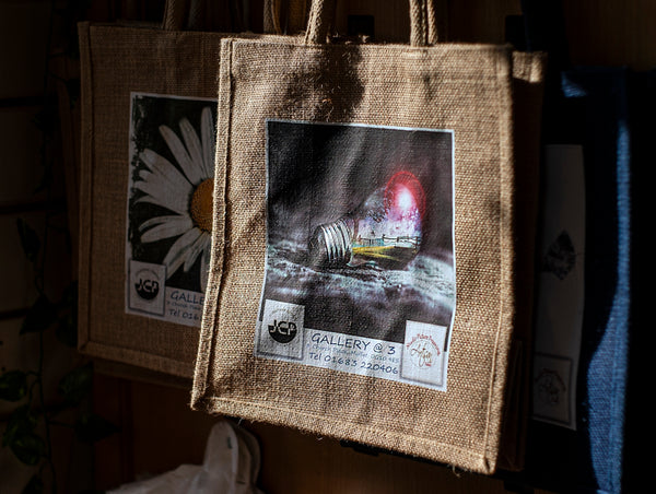 Jute bags with printed designs hanging in sunlight.